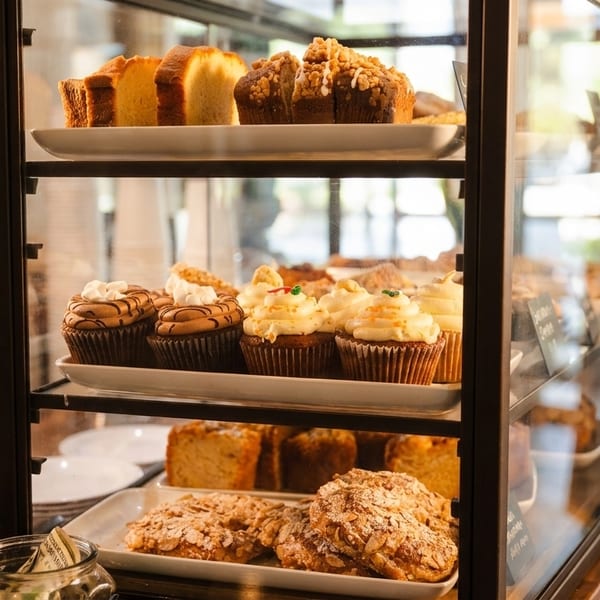Glass display case filled with various baked goods, including cupcakes, muffins, and pastries.