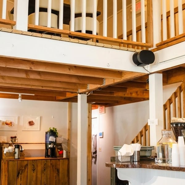 Interior of a cafe with a coffee bar, wine shelves, and wooden stairs leading to a second floor.