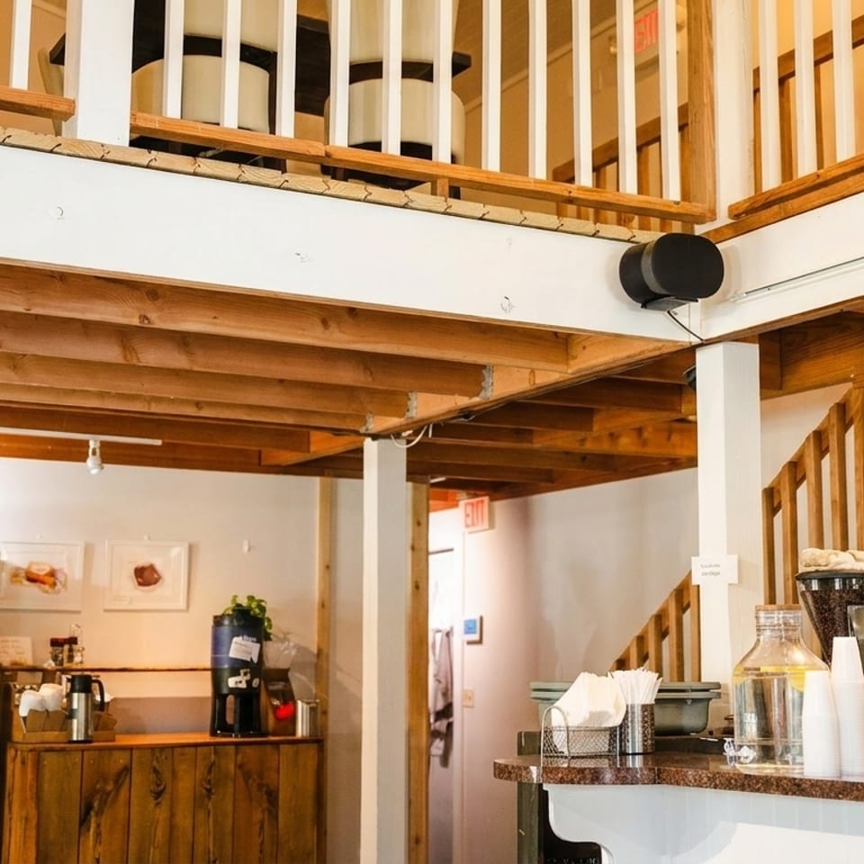 Interior of a cafe with a coffee bar, wine shelves, and wooden stairs leading to a second floor.
